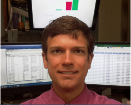 Portriate of Mr. Meeks in front of computer monitors displaying spreadsheets and charts.